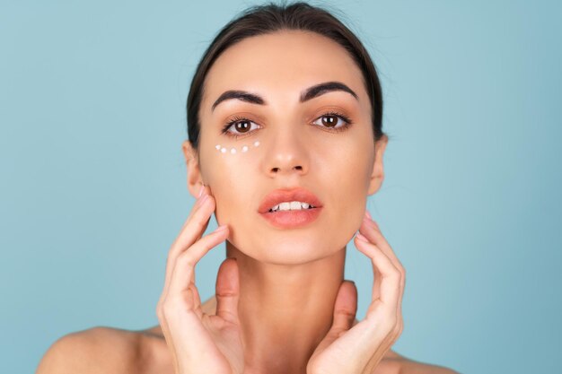 Retrato de primer plano de la belleza de una mujer en topless con piel perfecta y maquillaje natural, con puntos de crema anti-envejecimiento para hidratar y reafirmar la piel debajo de los ojos