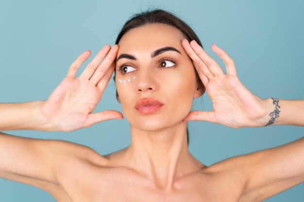 Retrato de primer plano de la belleza de una mujer en topless con piel perfecta y maquillaje natural, con puntos de crema anti-envejecimiento para hidratar y reafirmar la piel debajo de los ojos