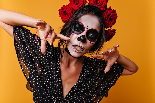 Foto gratuita retrato de primer plano de bruja mexicana con la cara pintada. mujer posando en estudio naranja.