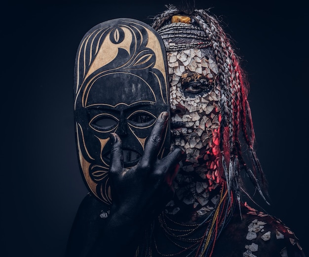 Retrato de primer plano de una bruja de la tribu indígena africana, vestida con traje tradicional. Concepto de maquillaje. Aislado en un fondo oscuro.
