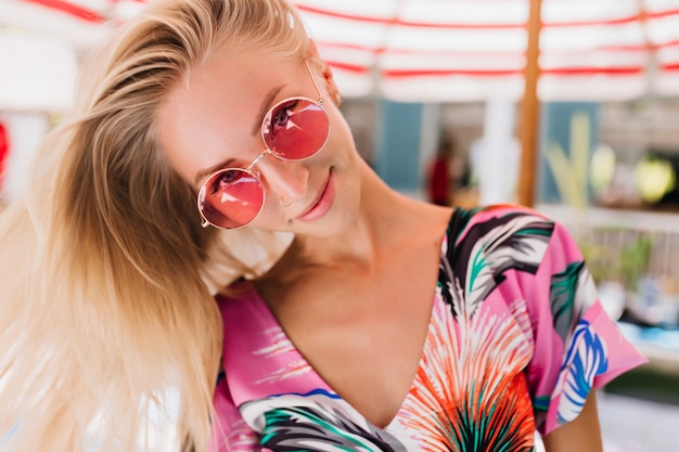 Retrato de primer plano de una chica increíble con gafas rosas divirtiéndose en el resort de verano.