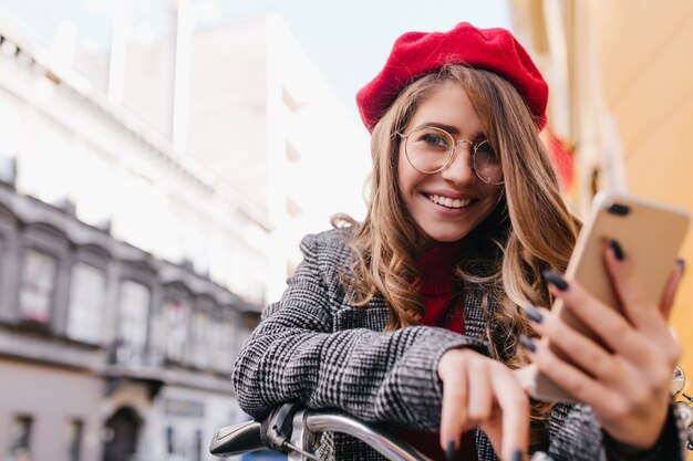 Retrato de primer plano de chica sensual en mensaje de texto de gafas grandes, sentado en bicicleta