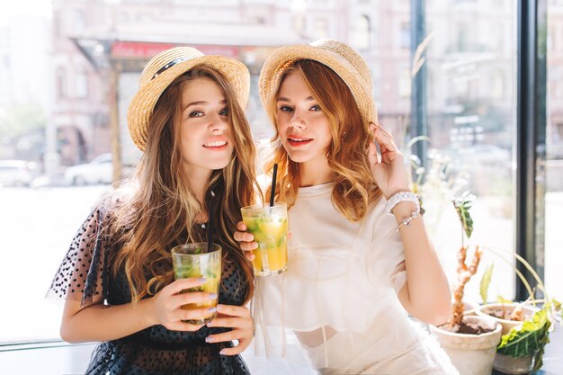 Retrato de primer plano de chicas cansadas pero felices disfrutando de cócteles después de ir de compras en fin de semana