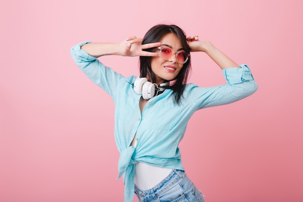 Retrato de primer plano de elegante joven asiática lleva gafas elegantes y camisa de algodón. adorable niña hispana con cabello negro brillante relajante en habitación rosa.