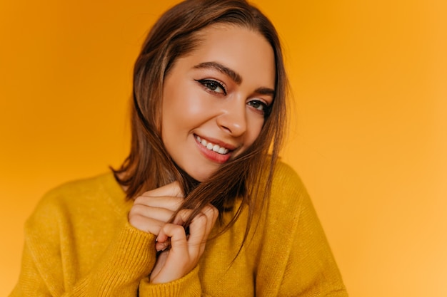 Foto gratuita retrato de primer plano de elegante modelo femenino con cabello castaño corto. foto interior de una hermosa niña caucásica sonriendo en la pared amarilla.