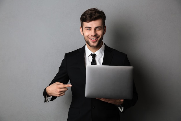 Retrato de primer plano del empresario alegre apuntando con el dedo en su computadora portátil,