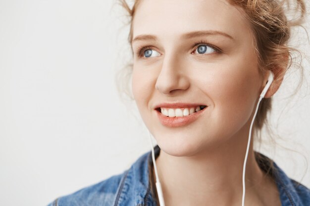 Retrato de primer plano de la encantadora chica de jengibre europeo mirando a un lado con expresión segura y amable mientras escucha música