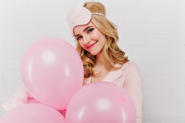 Retrato de primer plano de la encantadora cumpleañera disfrutando de la mañana. Encantadora mujer sonriente en antifaz celebrando algo con globos.