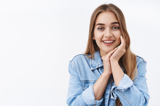 Retrato de primer plano encantadora joven con cabello rubio, suspirando tiernamente sonriendo y contemplando algo hermoso, toque suavemente la mejilla