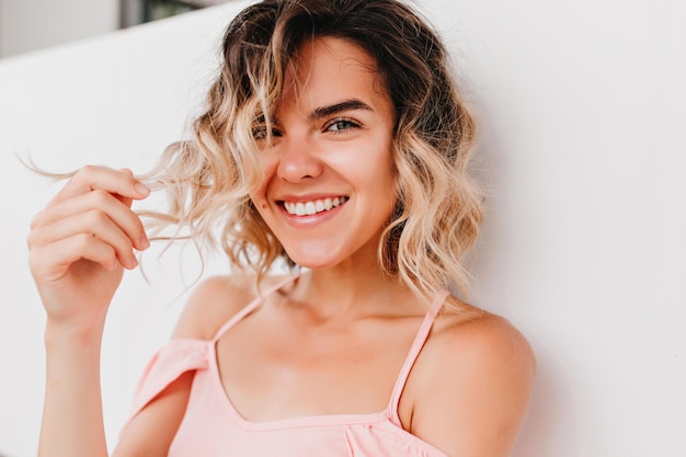 Retrato de primer plano de una encantadora niña riendo jugando con el pelo ondulado Foto de una mujer bronceada interesada con una bonita sonrisa