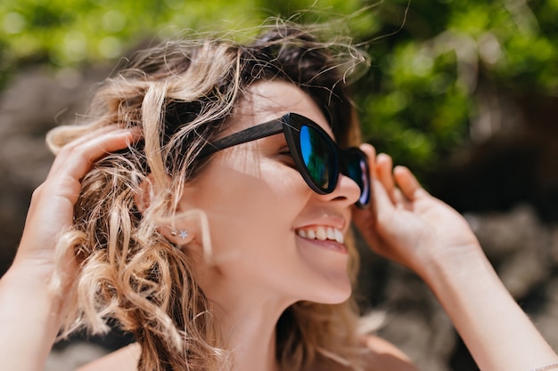 Retrato de primer plano de fascinante mujer emocional posando en la naturaleza. Foto al aire libre de dama elegante con gafas brillantes de moda.