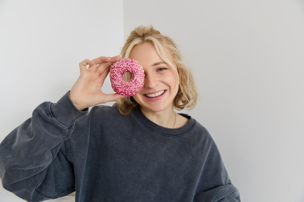 Foto gratuita retrato en primer plano de una feliz mujer rubia con una rosquilla en la mano comiendo comida dulce y deliciosa.