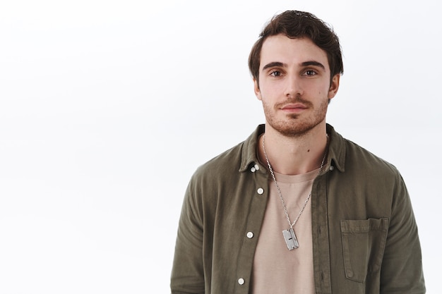 Retrato de primer plano de guapo joven sonriente con barba y bigote de pie en traje casual con expresión normal