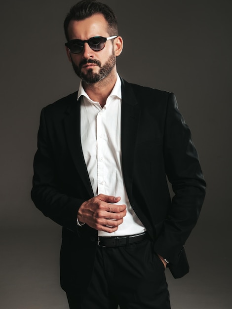 Foto gratuita retrato de primer plano de guapo modelo lambersexual con estilo inconformista seguro hombre moderno sexy vestido con elegante traje negro hombre de moda posando en estudio sobre fondo oscuro en gafas de sol