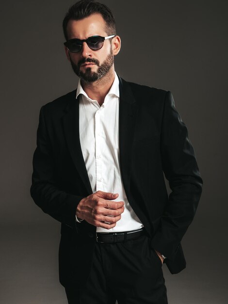 Retrato de primer plano de guapo modelo lambersexual con estilo inconformista seguro Hombre moderno sexy vestido con elegante traje negro Hombre de moda posando en estudio sobre fondo oscuro En gafas de sol