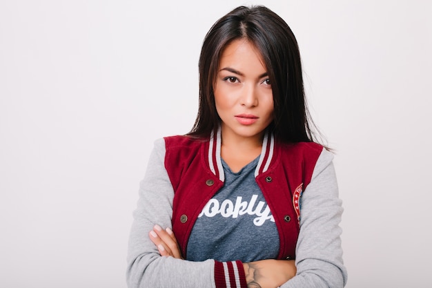 Retrato de primer plano de una hermosa chica asiática con ojos de color marrón oscuro de pie en pose de confianza frente a la pared blanca. Foto interior de maravillosa mujer joven con peinado corto posando con los brazos cruzados.