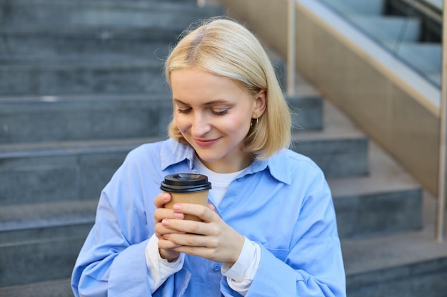 Foto gratuita retrato en primer plano de una hermosa estudiante rubia sonriente sentada en las escaleras fuera del campus