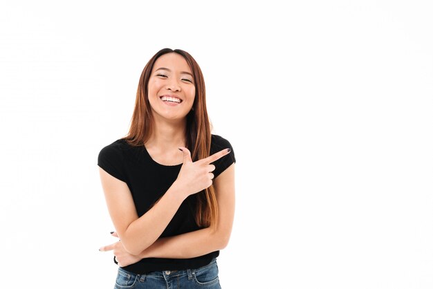 Retrato de primer plano de hermosa mujer asiática joven sonriente apuntando con el dedo, mirando a la cámara