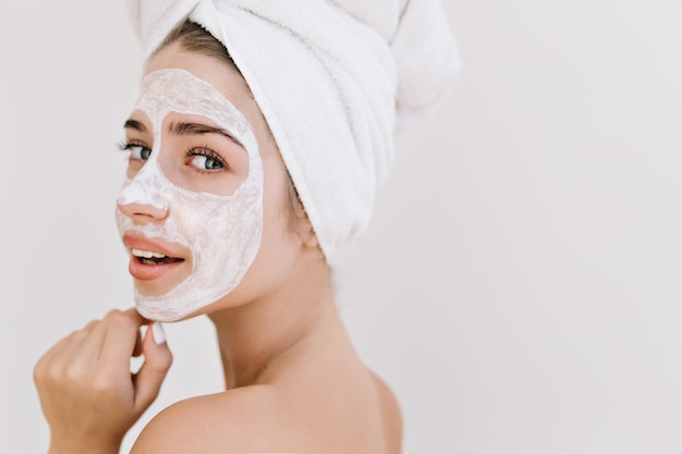 Foto gratuita retrato de primer plano de hermosa mujer joven con toallas después de tomar el baño hacer mascarilla cosmética en su rostro. rejuvenecimiento, cosmetología, hidratación y cuidado del rostro. spa. piel limpia y perfecta fondo blanco