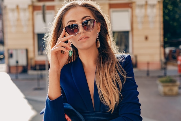 Foto gratuita retrato de primer plano de hermosa mujer vestida con elegante chaqueta azul caminando en la calle soleada de otoño con elegantes gafas de sol