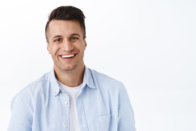 Retrato de primer plano de un hombre adulto guapo con una sonrisa radiante, satisfecho, se siente optimista y entusiasta, de pie pared blanca alegre, disfrutando del día, siente emoción