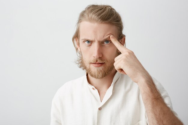 Retrato de primer plano de hombre barbudo atractivo serio con cabello rubio, levantando la ceja con el dedo índice como si tratara de amenazar o asustar a alguien