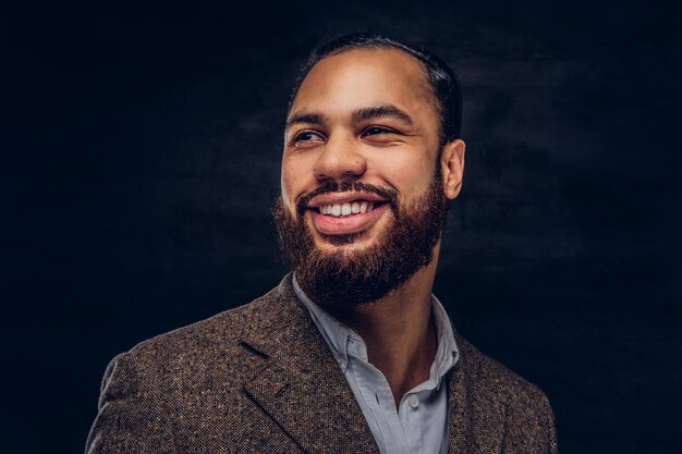 Retrato de primer plano de un hombre de negocios afroamericano barbudo guapo y sonriente con una chaqueta clásica marrón. Aislado en un fondo oscuro.