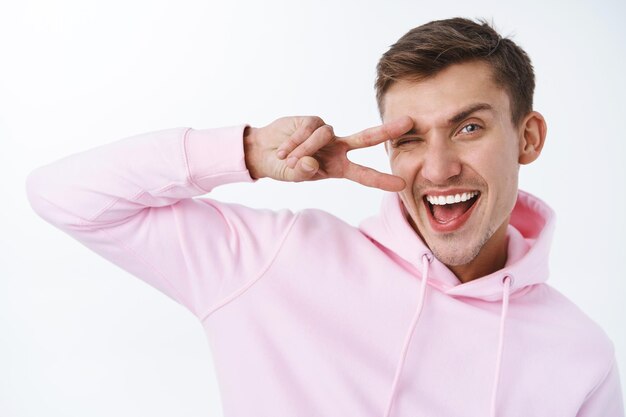 Retrato de primer plano de hombre rubio guapo optimista en sudadera con capucha rosa, ojos azules, sueño vivo, mantenerse positivo