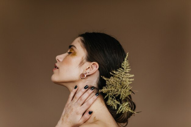 Retrato de primer plano de una increíble chica morena. Atractiva mujer caucásica posando con planta en el pelo.