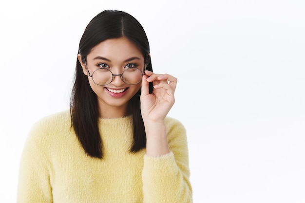 Retrato de primer plano interesada atractiva mujer asiática en gafas, mirando por debajo de las gafas sonriendo entretenido