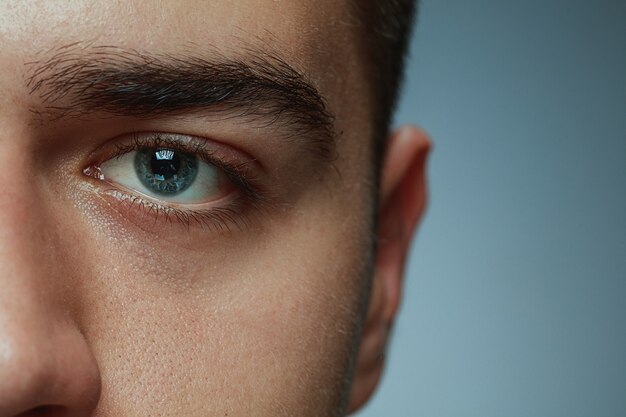 Retrato de primer plano de joven aislado sobre fondo gris de estudio. La cara y el ojo azul del modelo masculino caucásico. Concepto de salud y belleza de los hombres, cuidado personal, cuidado del cuerpo y la piel, medicina o psicología.