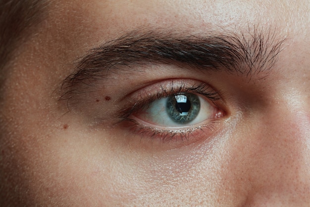 Retrato de primer plano de joven aislado sobre fondo gris de estudio. La cara y el ojo azul del modelo masculino caucásico. Concepto de salud y belleza de los hombres, cuidado personal, cuidado del cuerpo y la piel, medicina o psicología.