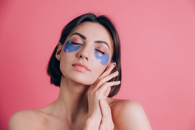 Retrato de primer plano de una joven y bella mujer en topless hombros abiertos con almohadillas de colágeno azul debajo de los ojos. Concepto de belleza.