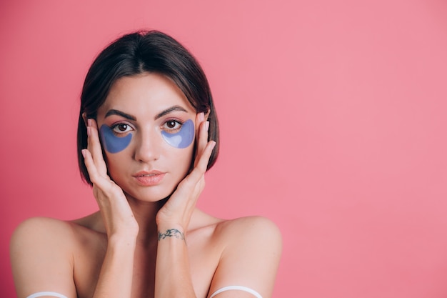 Retrato de primer plano de una joven y bella mujer en topless hombros abiertos con almohadillas de colágeno azul debajo de los ojos. Concepto de belleza.