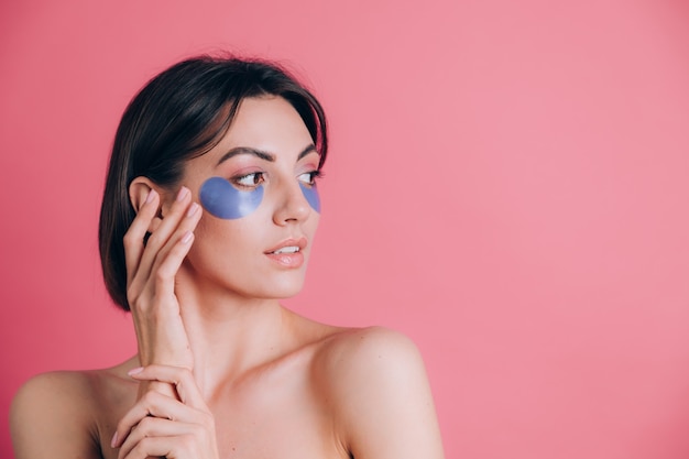 Retrato de primer plano de una joven y bella mujer en topless hombros abiertos con almohadillas de colágeno azul debajo de los ojos. Concepto de belleza.