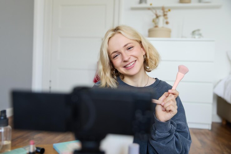 Foto gratuito retrato en primer plano de una joven blogger de belleza feliz que graba un vlog de estilo de vida en su habitación usando una cámara con