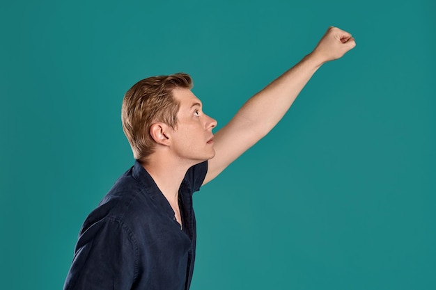 Foto gratuita retrato de primer plano de un joven buen compañero de jengibre con una elegante camiseta azul marino que actúa como si fuera un superhombre mientras posa en el fondo azul del estudio. expresiones faciales humanas. concepto de emociones sinceras. policía