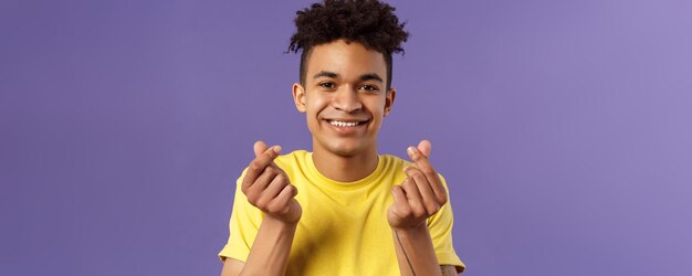 Retrato de primer plano de un joven encantador y lindo con corte de pelo afro que muestra signos de dedo del corazón coreano y sm