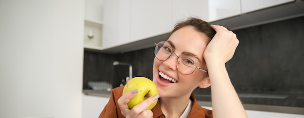 Foto gratuita retrato en primer plano de una joven feliz y elegante en casa mordiendo una manzana comiendo frutas en casa