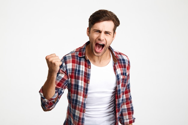 Retrato de primer plano de joven gritando en camisa a cuadros hace gesto ganador, mirando