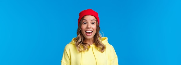 Foto gratuita retrato de primer plano de una joven hipster emocionada e intrigada con gorro rojo y sudadera con capucha amarilla jadeando