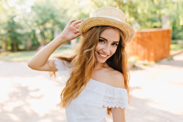 Retrato de primer plano de una joven inspirada con hermosos ojos con sombrero de paja. Chica rubia romántica con piel pálida posando