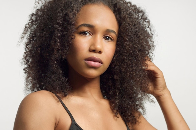 Retrato de primer plano de una joven modelo de raza mixta con cabello rizado en estudio con maquillaje neutral natural con cabello afro rizado grande