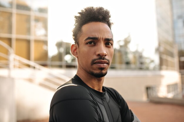 Retrato de primer plano de un joven moreno de piel oscura en camiseta negra deportiva parece recta