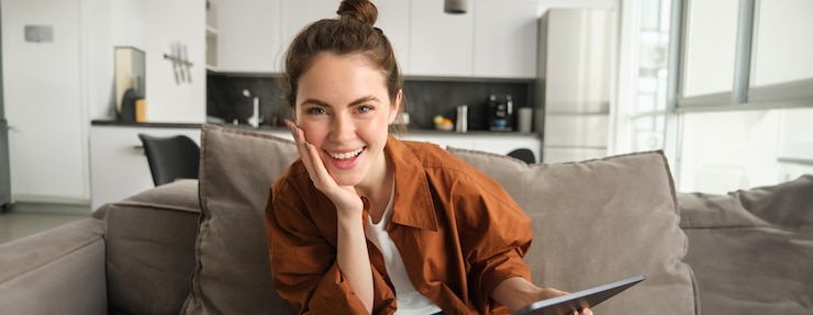 Foto gratuito retrato en primer plano de una joven mujer moderna sentada en el sofá y usando una tableta digital leyendo un libro electrónico