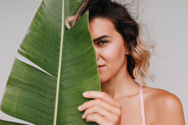 Retrato de primer plano de una linda chica europea con un corte de pelo corto aislado en un fondo claro Foto de una encantadora dama escondida detrás de una gran planta