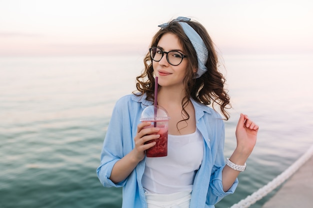 Retrato de primer plano de una linda chica inspirada en gafas disfruta de la brisa del mar temprano en la mañana