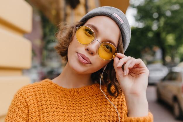 Retrato de primer plano de magnífica modelo femenina con pelo rizado posando delante de árboles en la mañana