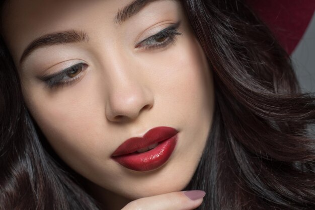 Retrato de primer plano de moda y modelo de moda mujer con sombrero rojo oscuro mirando a otro lado y posando para el fotógrafo en estudio.