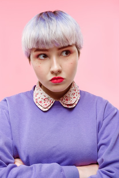 Foto gratuita retrato de primer plano de moda de niña dollish hermosa enojada con cabello violeta claro corto con suéter lila sobre pared rosa